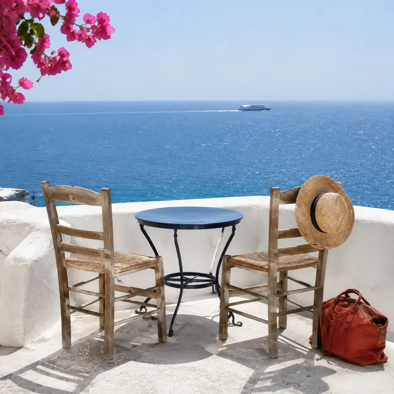 Two empty chairs and a table on a whitewashed terrace overlooking the sea